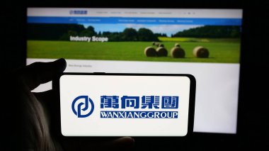 Stuttgart, Almanya - 03-19-2025: Çinli Wanxiang Group Corporation şirketinin logosunu elinde tutan kişi web sayfasının önünde ekranda. Telefon ekranına odaklan.
