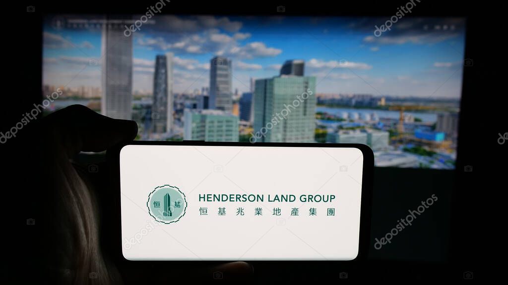 Stuttgart, Germany - 03-14-2025: Person holding cellphone with logo of company Henderson Land Development Co. Ltd. on screen in front of webpage. Focus on phone display.