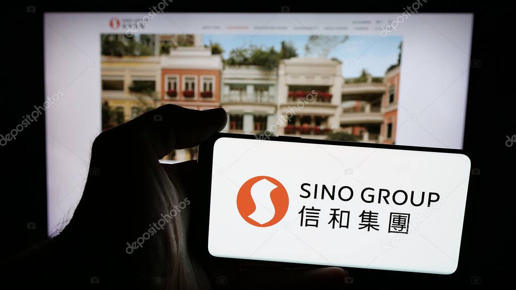 Stuttgart, Germany - 03-14-2025: Person holding mobile phone with logo of Hong Kong real estate company Sino Group on screen in front of web page. Focus on phone display.
