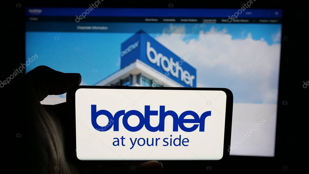 Stuttgart, Germany - 03-14-2025: Person holding cellphone with logo of electronics company Brother Industries Ltd. on screen in front of webpage. Focus on phone display.