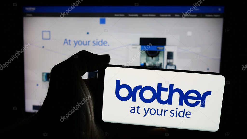 Stuttgart, Germany - 03-14-2025: Person holding mobile phone with logo of electronics company Brother Industries Ltd. on screen in front of web page. Focus on phone display.