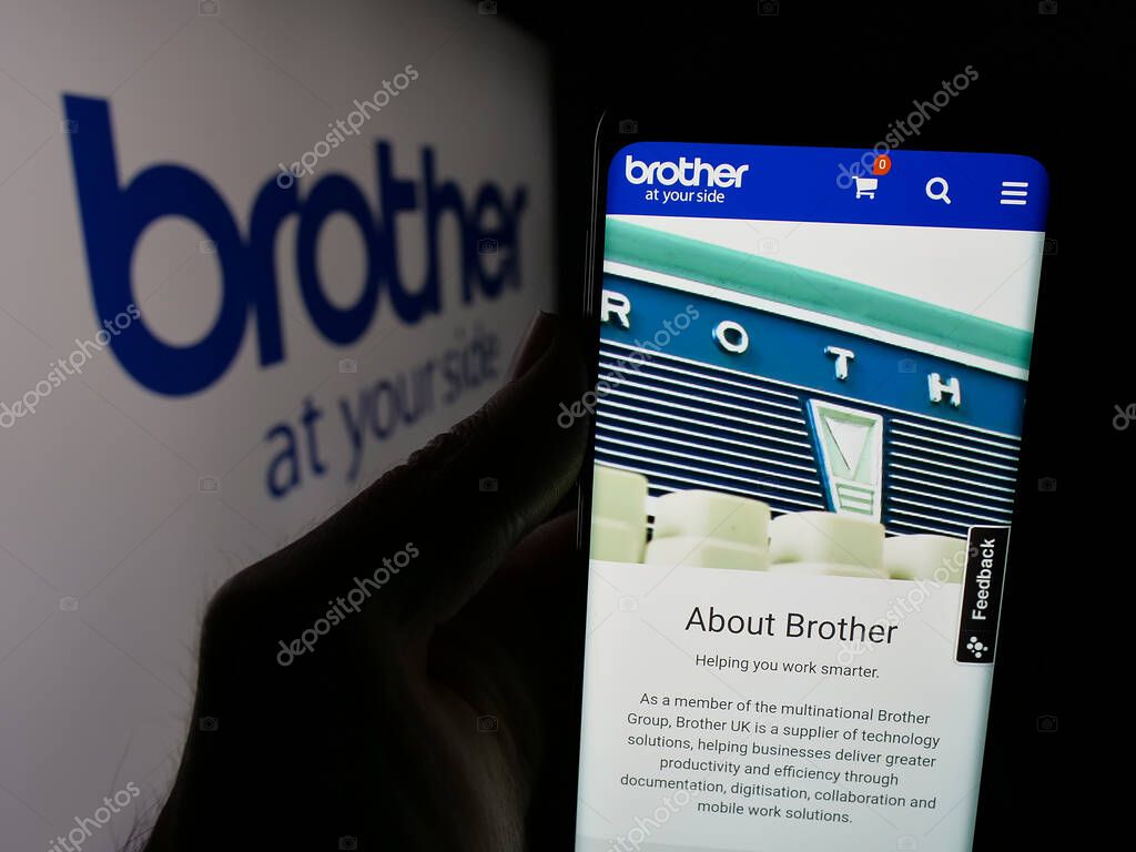 Stuttgart, Germany - 03-14-2025: Person holding web page with logo of electronics company Brother Industries Ltd. on screen in front of logo. Focus on center of phone display.