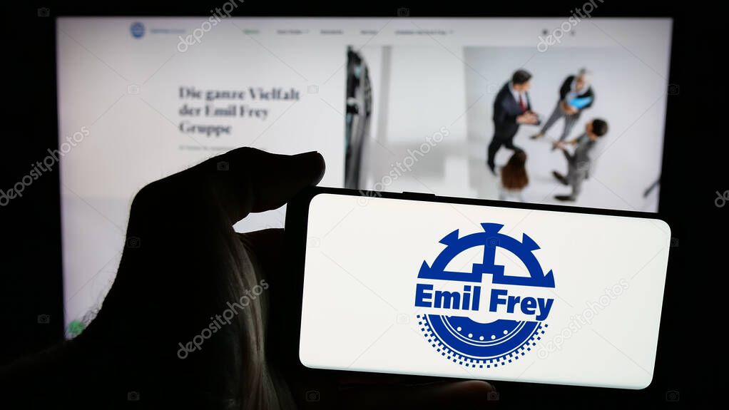 Stuttgart, Germany - 03-18-2025: Person holding mobile phone with logo of Swiss automotive company Emil Frey Holding AG on screen in front of web page. Focus on phone display.