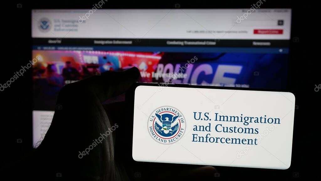 Stuttgart, Germany - 03-18-2025: Person holding mobile phone with logo of US Immigration and Customs Enforcement (ICE) on screen in front of web page. Focus on phone display.