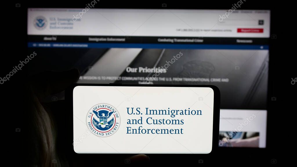 Stuttgart, Germany - 03-18-2025: Person holding cellphone with logo of US Immigration and Customs Enforcement (ICE) on screen in front of webpage. Focus on phone display.