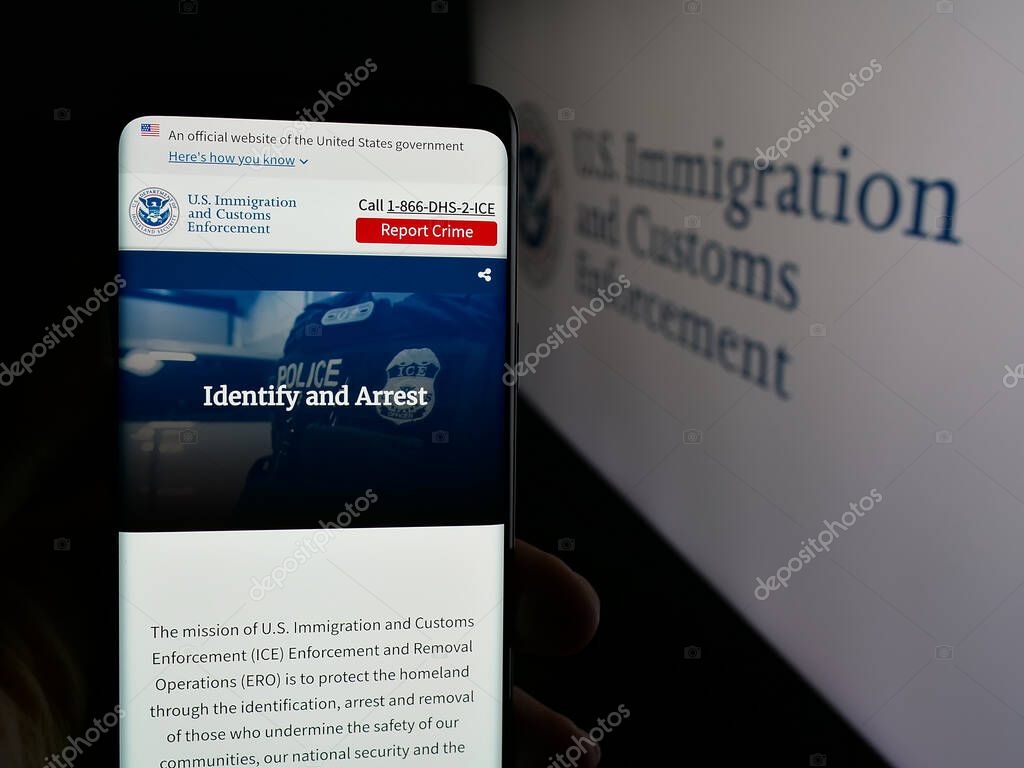 Stuttgart, Germany - 03-18-2025: Person holding cellphone with webpage of US Immigration and Customs Enforcement (ICE) on screen in front of logo. Focus on center of phone display.