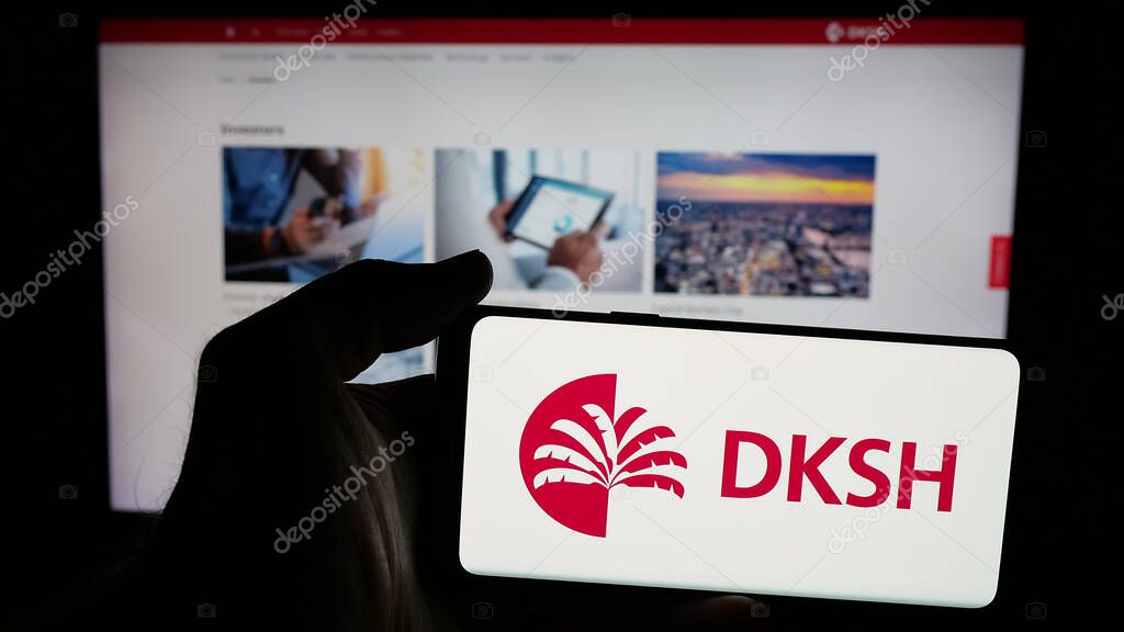 Stuttgart, Germany - 03-19-2025: Person holding mobile phone with logo of Swiss outsourcing company DKSH Holding AG on screen in front of web page. Focus on phone display.
