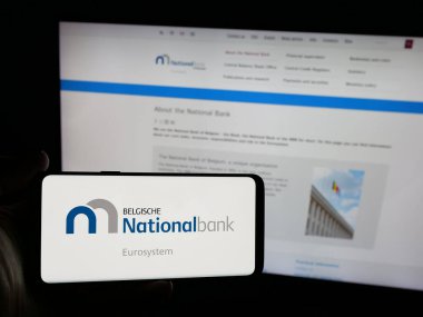 Stuttgart, Almanya - 03-21-2025: İnternet sitesi önünde üzerinde Belçika Ulusal Bankası van Belgie (NBB) logosu bulunan akıllı telefon sahibi kişi. Telefon ekranına odaklan.
