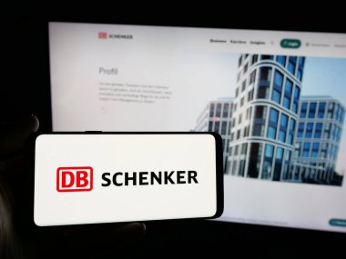 Stuttgart, Almanya - 03-21-2025: Alman lojistik şirketi DB Schenker 'in logosunu elinde tutan kişi web sitesinin önünde ekranda. Telefon ekranına odaklan.