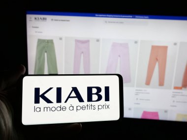 Stuttgart, Almanya - 03-21-2025: Fransız moda perakende şirketi Kiabi 'nin logosuna sahip akıllı telefon sahibi kişi web sitesinin önünde ekranda. Telefon ekranına odaklan.