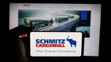 Stuttgart, Almanya - 03-24-2025: Alman karavan şirketi Schmitz Cargobull AG 'nin logosunu elinde tutan kişi web sayfasının önünde ekranda. Telefon ekranına odaklan.