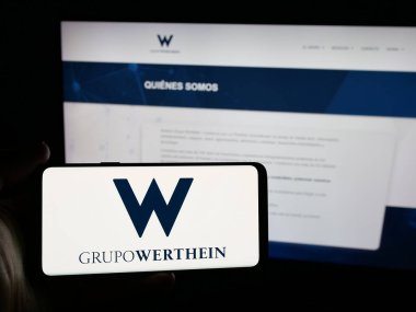 Stuttgart, Almanya - 03-24-2025: Arjantinli şirket Grupo Werthein 'in logosunu elinde tutan kişi web sitesinin önünde ekranda. Telefon ekranına odaklan.