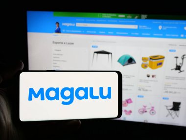 Stuttgart, Almanya - 03-24-2025: İnternet sitesinin önünde perakende şirketi Luiza S.A. 'nın (Magalu) logosuna sahip akıllı telefon sahibi kişi. Telefon ekranına odaklan.