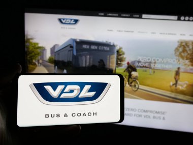 Stuttgart, Almanya - 03-24-2025: Hollandalı otomotiv şirketi VDL Otobüs ve Koç 'un logosunu elinde tutan kişi web sitesinin önünde ekranda. Telefon ekranına odaklan.