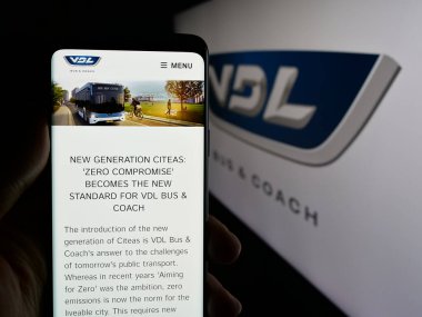 Stuttgart, Almanya - 03-24-2025: Hollandalı otomotiv şirketi VDL Otobüs ve Koç 'un internet sayfası logonun önünde duran kişi. Telefon ekranının merkezine odaklan.
