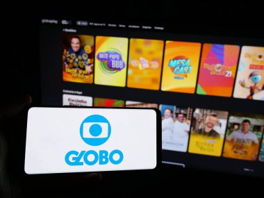 Stuttgart, Almanya - 03-27-2025: Brezilyalı televizyon kanalı Globo 'nun logosunu elinde tutan kişi web sitesinin önünde ekranda. Telefon ekranına odaklan.
