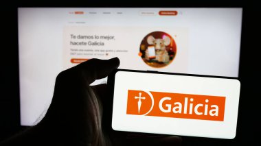 Stuttgart, Almanya - 03-27-2025: Üzerinde bankacılık şirketi Grupo Financiero Galicia 'nın logosu olan cep telefonu sahibi kişi web sayfasının önünde ekranda. Telefon ekranına odaklan.