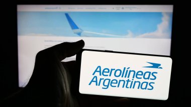 Stuttgart, Almanya - 03-27-2025: Web sayfası önünde ekranda Aerolineas Argentinas S.A. havayolu şirketinin logosunun bulunduğu cep telefonu sahibi kişi. Telefon ekranına odaklan.