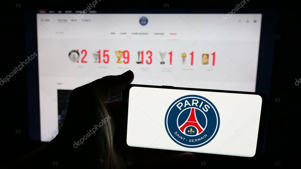 Stuttgart, Germany - 03-21-2025: Person holding mobile phone with logo of Paris Saint-Germain Football Club (PSG) on screen in front of web page. Focus on phone display.