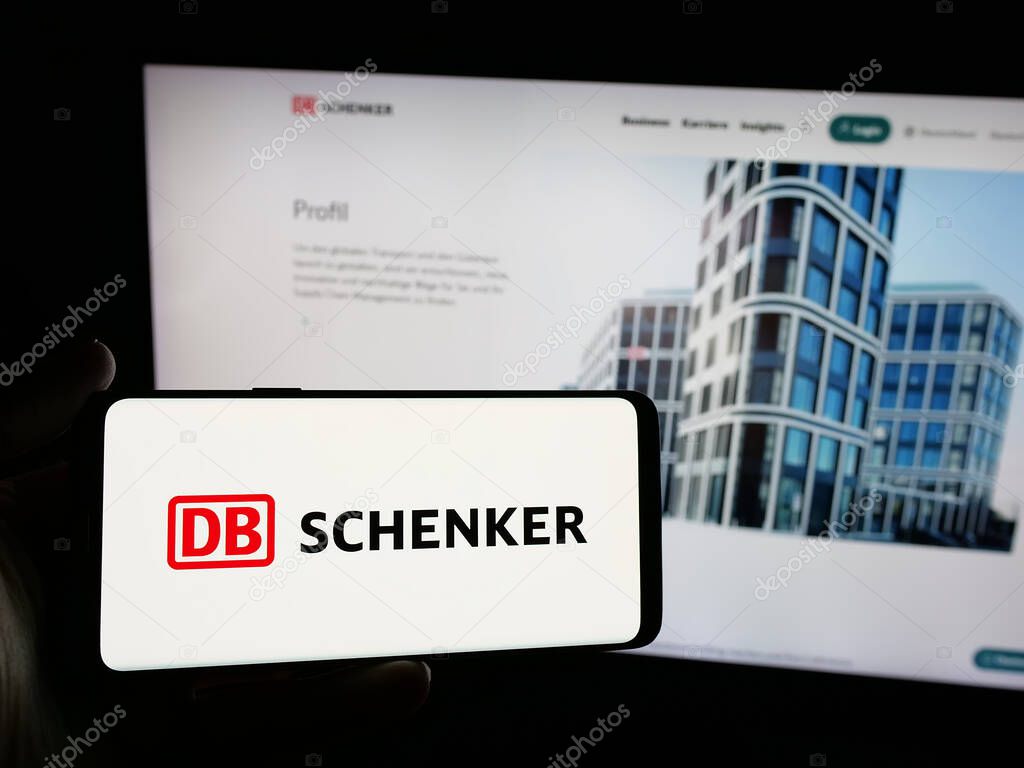 Stuttgart, Germany - 03-21-2025: Person holding smartphone with logo of German logistics company DB Schenker on screen in front of website. Focus on phone display.
