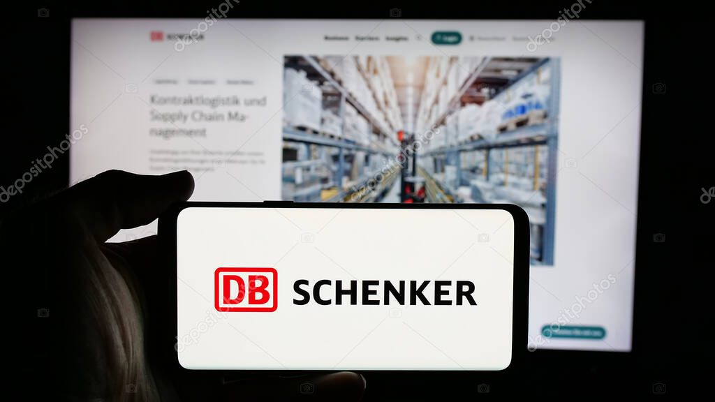 Stuttgart, Germany - 03-21-2025: Person holding cellphone with logo of German logistics company DB Schenker on screen in front of webpage. Focus on phone display.