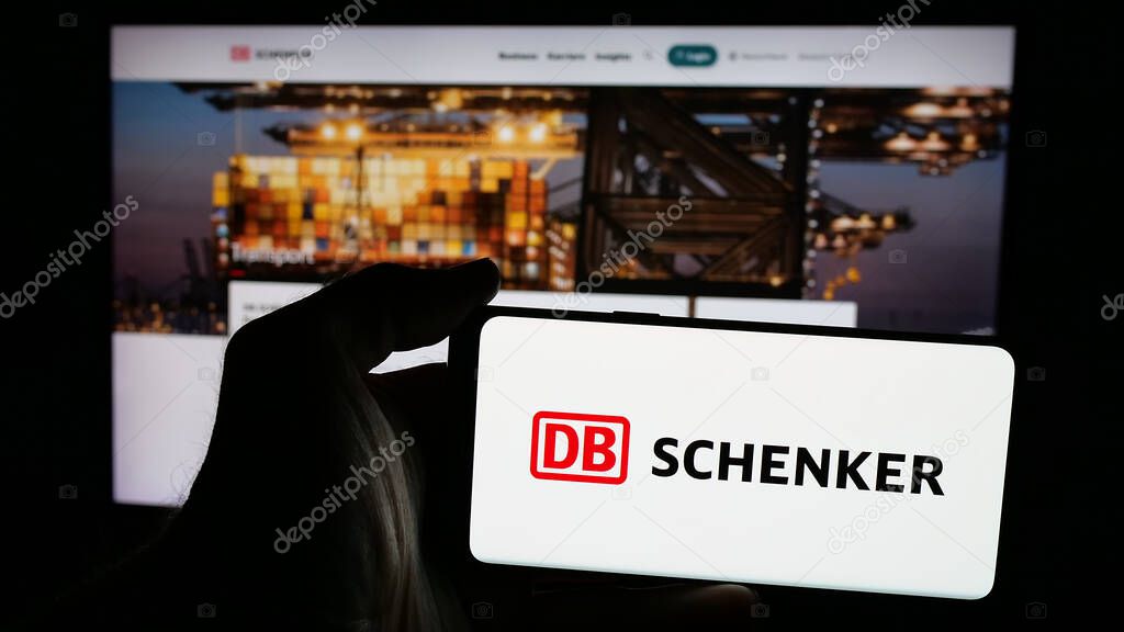 Stuttgart, Germany - 03-21-2025: Person holding mobile phone with logo of German logistics company DB Schenker on screen in front of web page. Focus on phone display.