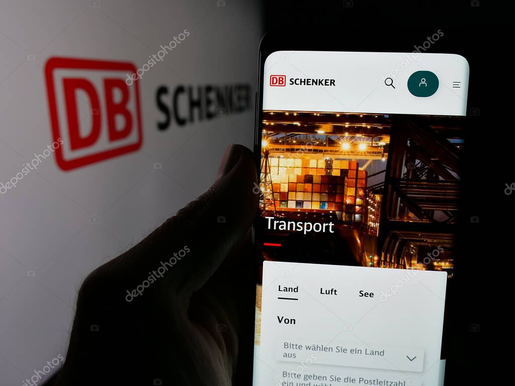 Stuttgart, Germany - 03-21-2025: Person holding web page with logo of German logistics company DB Schenker on screen in front of logo. Focus on center of phone display.
