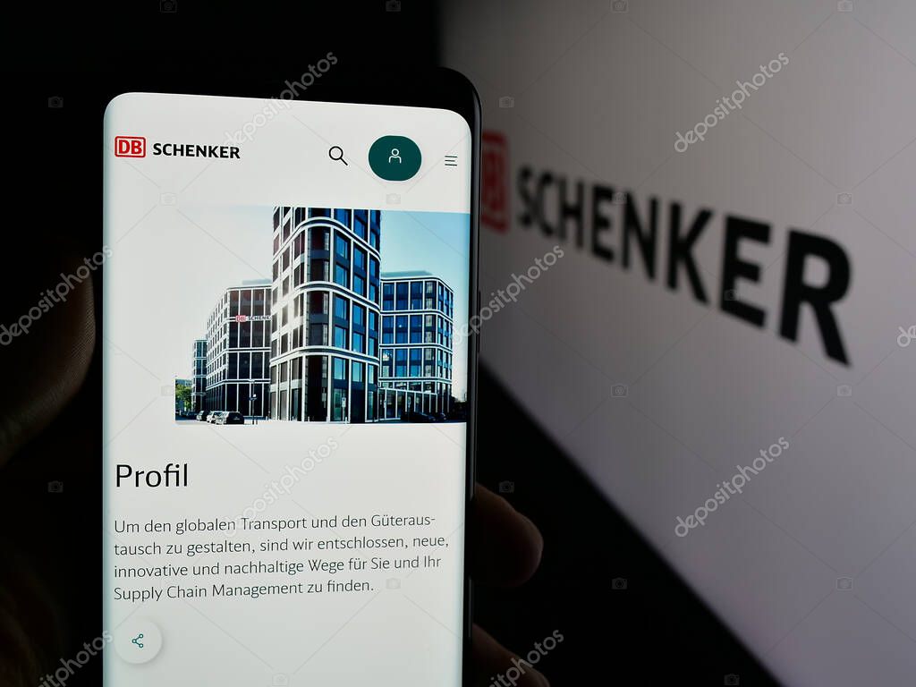 Stuttgart, Germany - 03-21-2025: Person holding cellphone with webpage of German logistics company DB Schenker on screen in front of logo. Focus on center of phone display.