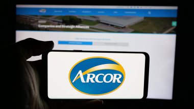 Stuttgart, Almanya - 03-27-2025: Şekerleme şirketi Arcor S.A.I.C. logosuyla cep telefonu tutan kişi Web sayfasının önünde ekranda. Telefon ekranına odaklan.