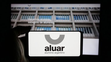 Stuttgart, Almanya - 03-31-2025: Aluar Aluminio Argentino S.A.I.C. şirketinin logosuyla cep telefonu tutan kişi Web sayfasının önünde ekranda. Telefon ekranına odaklan.