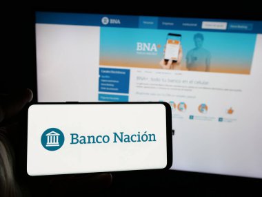 Stuttgart, Almanya - 03-31-2025: İnternet sitesi önünde Banco de la Nacion Argentina (BNA) şirketinin logosuna sahip akıllı telefon sahibi kişi. Telefon ekranına odaklan.