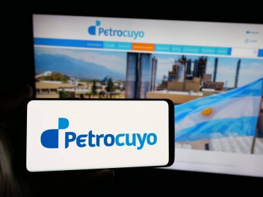 Stuttgart, Almanya - 03-31-2025: İnternet sitesi önünde Petroquimica Cuyo SAIC (Petrocuyo) şirketinin logosuna sahip akıllı telefon sahibi kişi. Telefon ekranına odaklan.