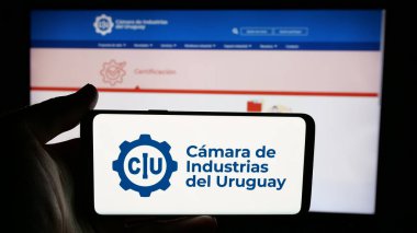 Stuttgart, Almanya - 04-02-2025: İnternet sayfası önünde ekranda Camara de Industrias del Uruguay örgütünün logosuna sahip cep telefonu sahibi kişi. Telefon ekranına odaklan.