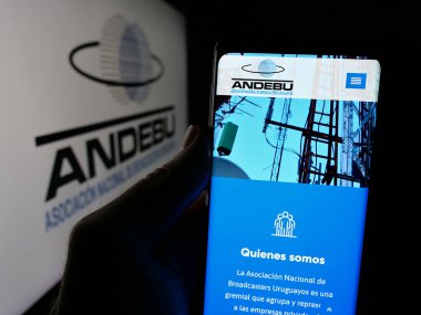 Stuttgart, Almanya - 04-03-2025: Logo önündeki ekranda Uruguay yayın derneği ANDEBU 'nun logosunun logosu bulunan kişi. Telefon ekranının merkezine odaklan.