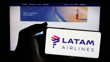 Stuttgart, Almanya - 04-03-2025: Web sayfası önünde üzerinde havayolu şirketi LATAM Airlines Chile logosu bulunan cep telefonu sahibi kişi. Telefon ekranına odaklan.