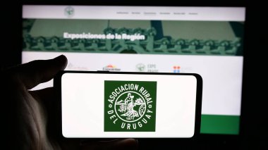 Stuttgart, Almanya - 04-03-2025: Web sayfasının önünde Asociacion Rural del Uruguay (ARU) logosu olan cep telefonu sahibi kişi. Telefon ekranına odaklan.