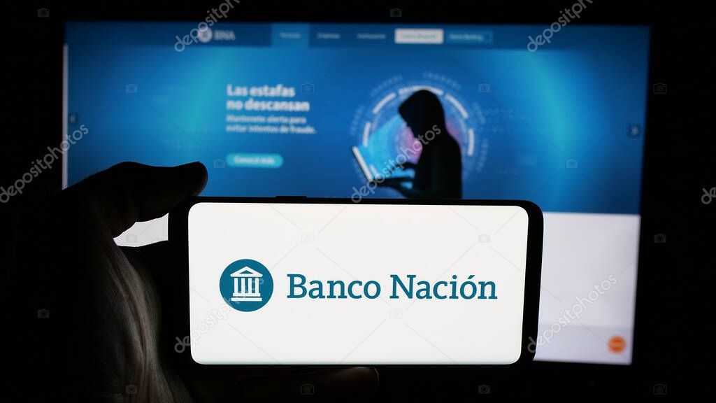 Stuttgart, Germany - 03-31-2025: Person holding cellphone with logo of company Banco de la Nacion Argentina (BNA) on screen in front of webpage. Focus on phone display.
