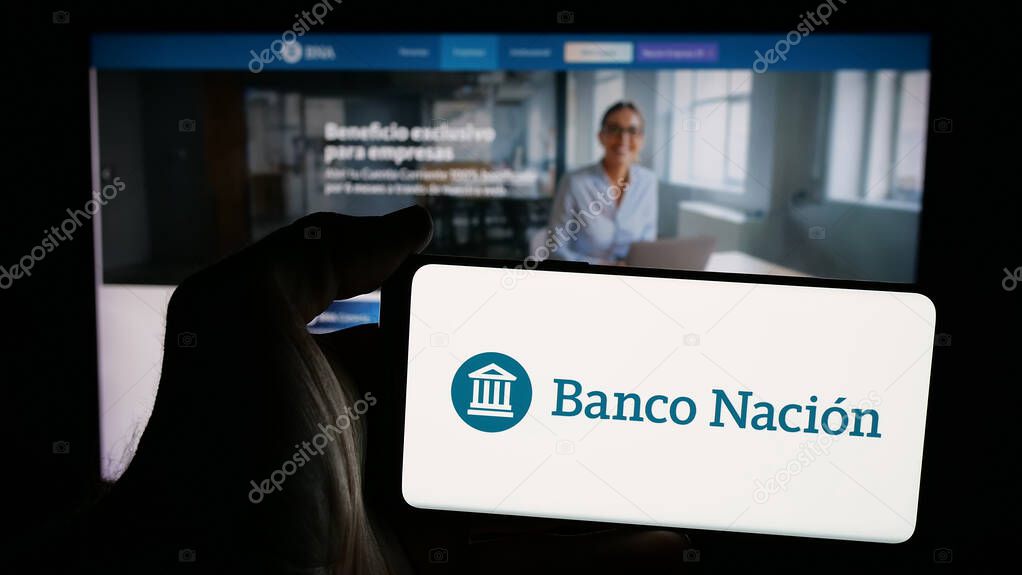 Stuttgart, Germany - 03-31-2025: Person holding mobile phone with logo of company Banco de la Nacion Argentina (BNA) on screen in front of web page. Focus on phone display.