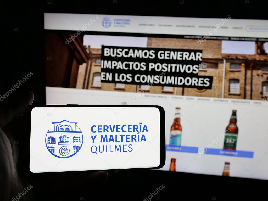 Stuttgart, Germany - 04-01-2025: Person holding smartphone with logo of brewing company Cerveceria y Malteria Quilmes on screen in front of website. Focus on phone display.