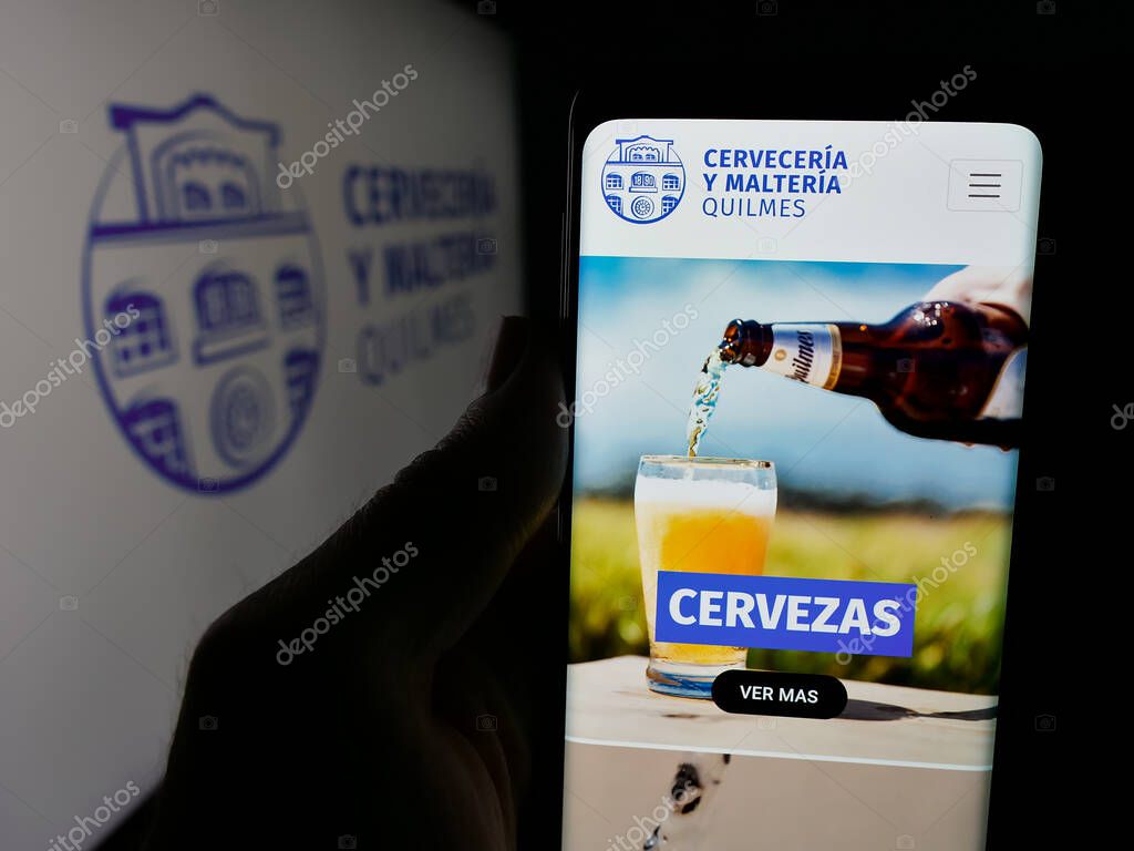 Stuttgart, Germany - 04-01-2025: Person holding web page with logo of brewing company Cerveceria y Malteria Quilmes on screen in front of logo. Focus on center of phone display.