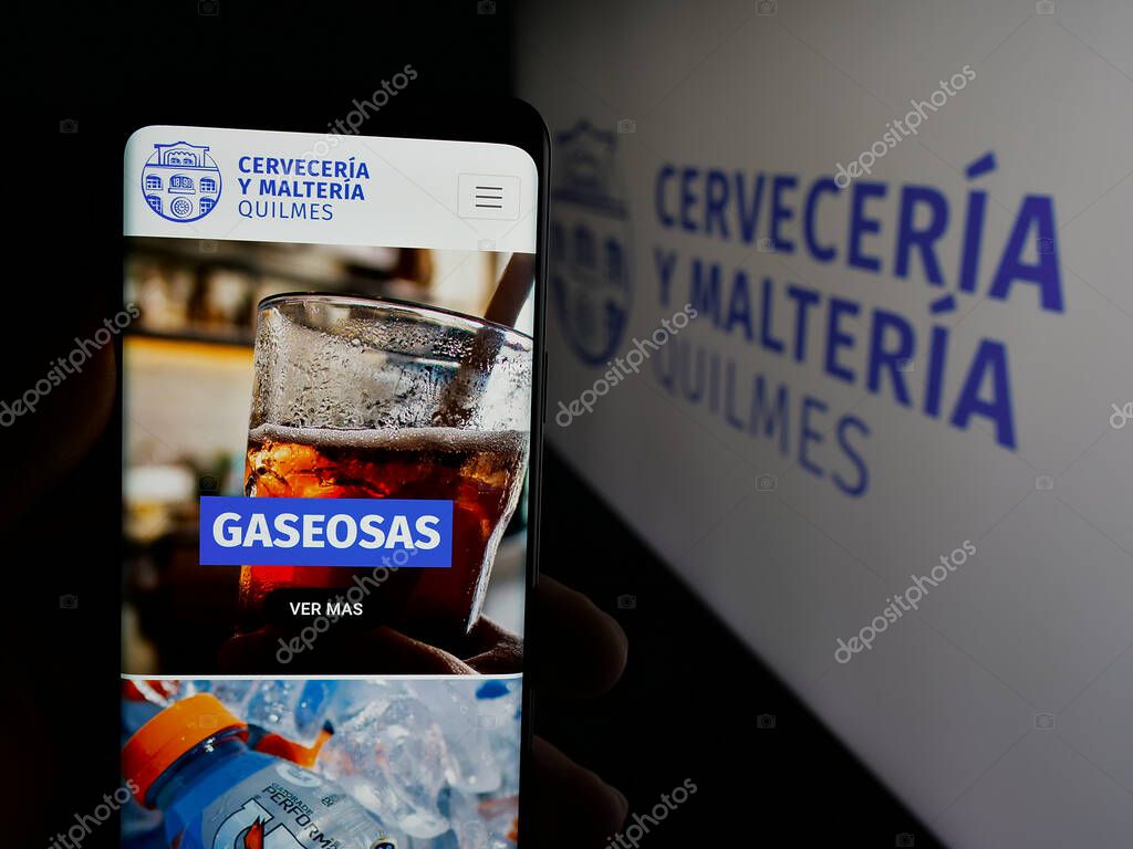 Stuttgart, Germany - 04-01-2025: Person holding cellphone with webpage of brewing company Cerveceria y Malteria Quilmes on screen in front of logo. Focus on center of phone display.