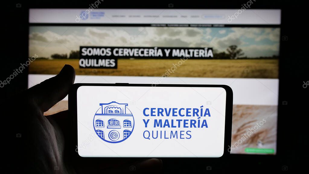 Stuttgart, Germany - 04-01-2025: Person holding cellphone with logo of brewing company Cerveceria y Malteria Quilmes on screen in front of webpage. Focus on phone display.