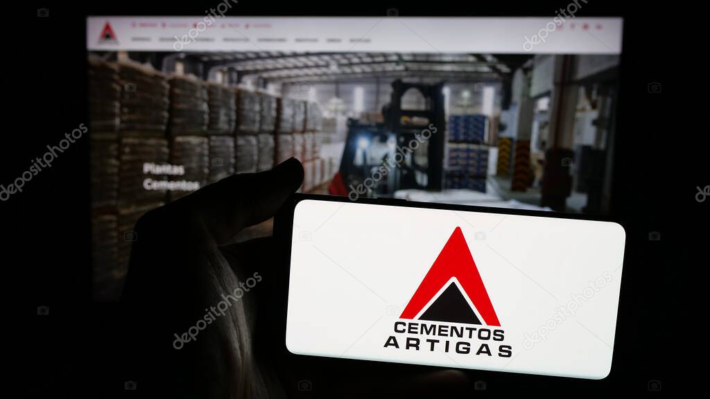 Stuttgart, Germany - 04-02-2025: Person holding mobile phone with logo of Uruguayan company Cementos Artigas S.A. on screen in front of web page. Focus on phone display.