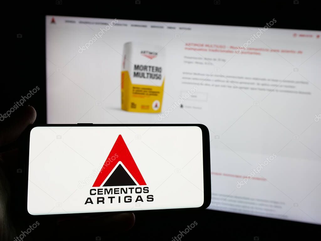 Stuttgart, Germany - 04-02-2025: Person holding smartphone with logo of Uruguayan company Cementos Artigas S.A. on screen in front of website. Focus on phone display.