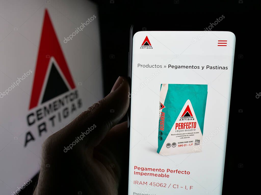 Stuttgart, Germany - 04-02-2025: Person holding web page with logo of Uruguayan company Cementos Artigas S.A. on screen in front of logo. Focus on center of phone display.