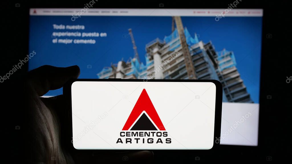 Stuttgart, Germany - 04-02-2025: Person holding cellphone with logo of Uruguayan company Cementos Artigas S.A. on screen in front of webpage. Focus on phone display.