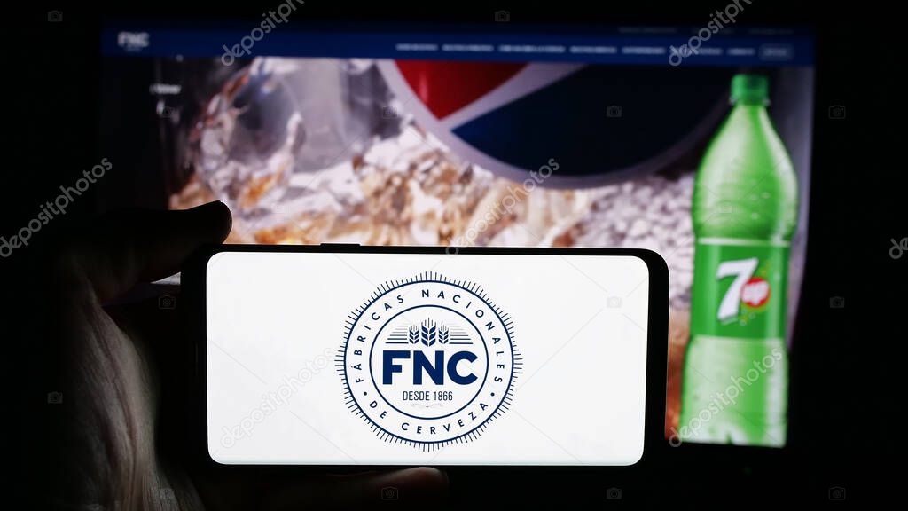Stuttgart, Germany - 04-03-2025: Person holding cellphone with logo of company Fabricas Nacionales de Cerveza (FNC) on screen in front of webpage. Focus on phone display.