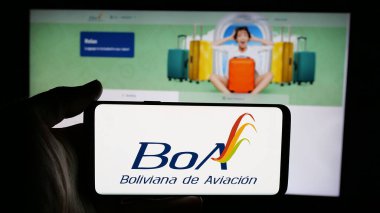 Stuttgart, Almanya - 04-07-2025: Web sayfası önünde Boliviana de Aviacion (BoA) havayolu şirketinin logosuyla cep telefonu tutan kişi. Telefon ekranına odaklan.