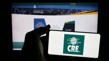 Stuttgart, Almanya - 04-09-2025: Web sayfasının önünde üzerinde Cooperativa Kırsal de Electrificacion (CRE) logosu bulunan cep telefonu sahibi kişi. Telefon ekranına odaklan.