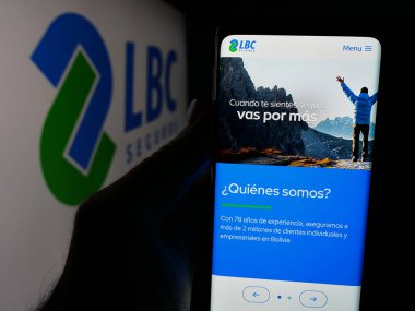 Stuttgart, Almanya - 04-09-2025: Bolivyalı sigorta şirketi LBC Seguros 'un web sayfası ile logo önünde cep telefonu tutan kişi. Telefon ekranının merkezine odaklan.